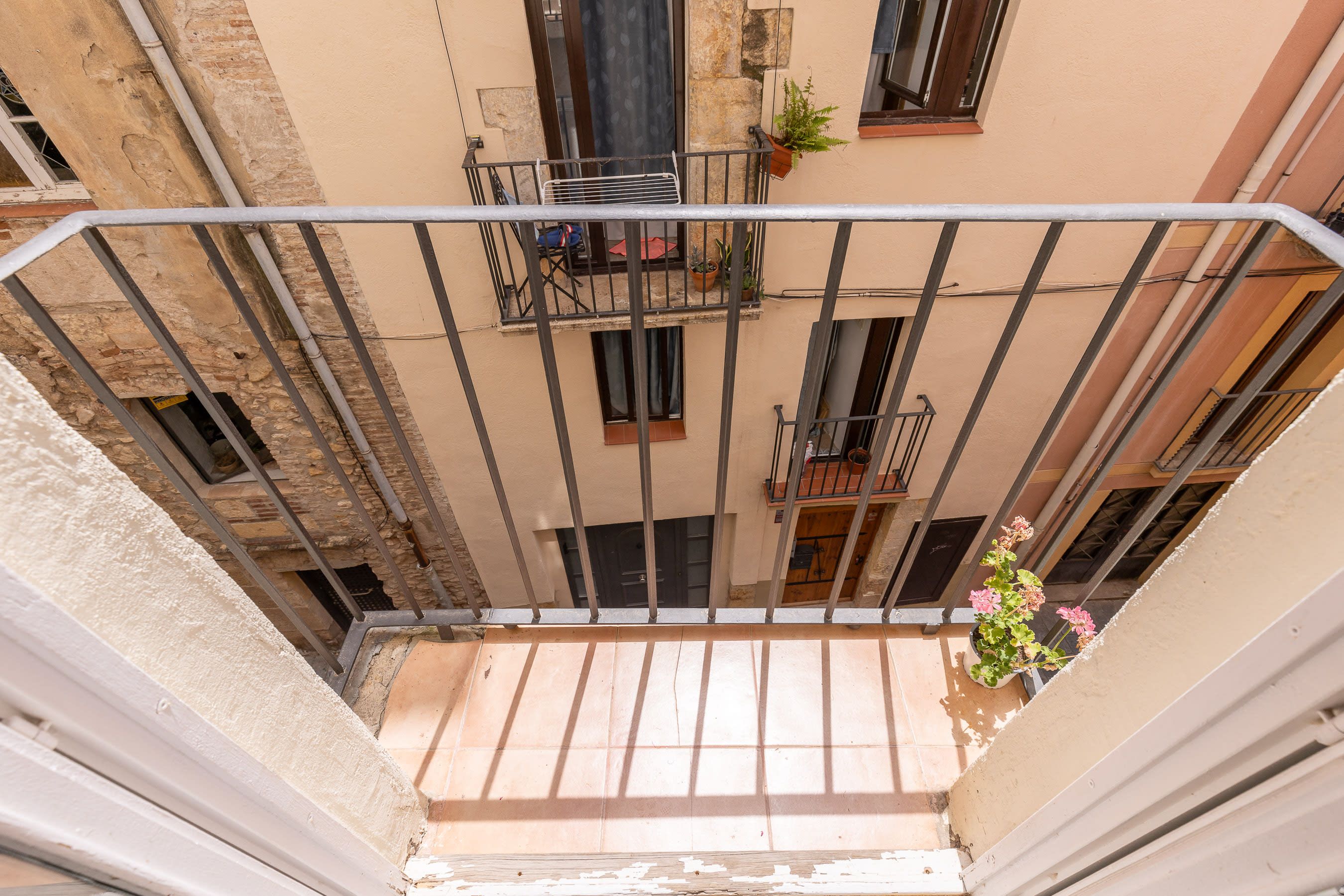 A narrow courtyard with a metal railing, potted plants, and a view of adjacent buildings.