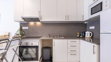 A compact kitchen with white cabinets, a stainless steel range, a built-in oven, a sink, and a coffee maker.