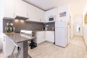 A modern kitchen with white cabinets, a stainless steel sink, a microwave, and a refrigerator. There is a dining table with chairs and a vase on the counter. - Old Town • Studio - Unik Vacation (Tarragona)