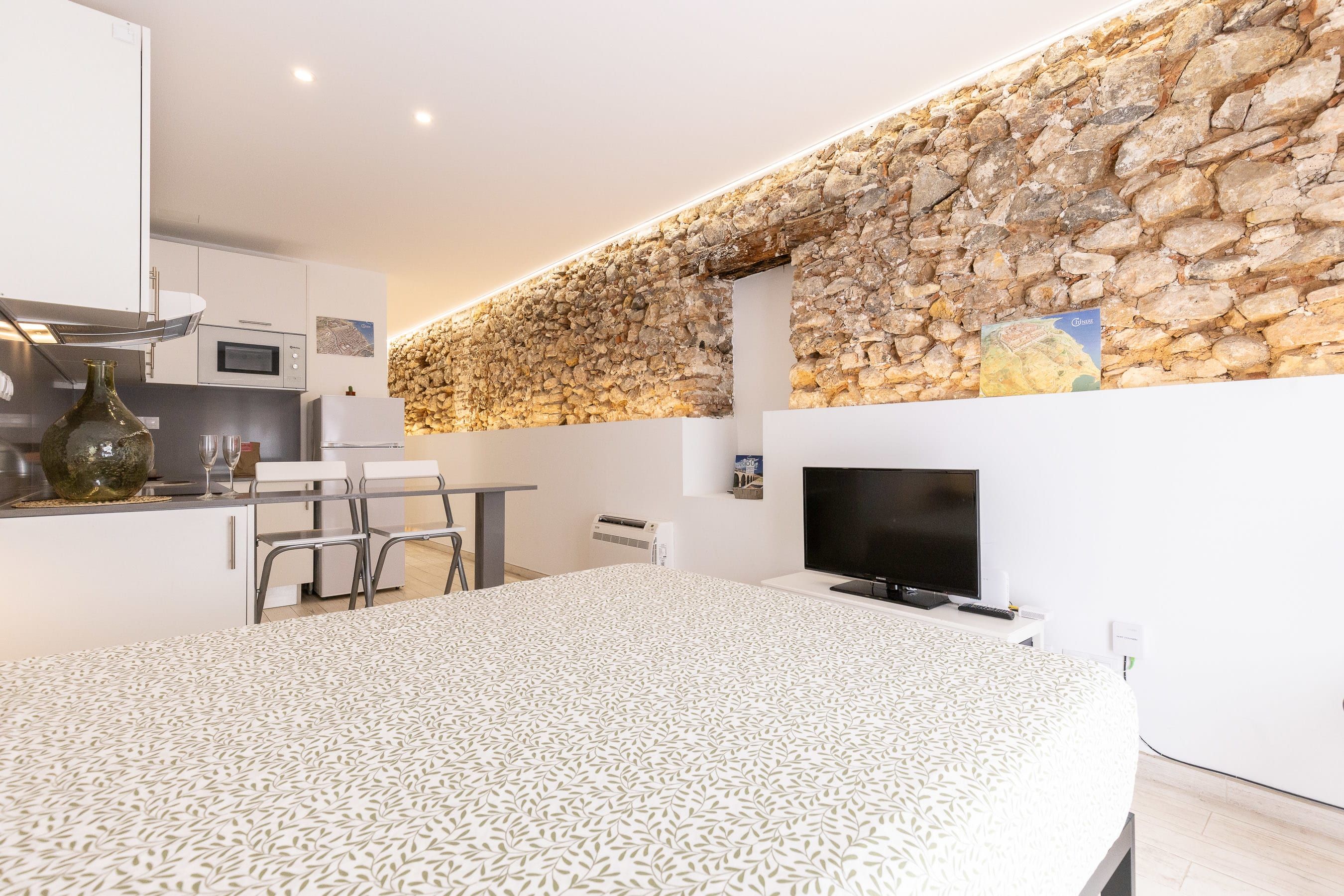 A modern kitchen with a stone wall, a dining area with a patterned tablecloth, and a flat-screen TV.