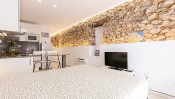 A modern kitchen with a stone wall, a dining area with a patterned tablecloth, and a flat-screen TV.