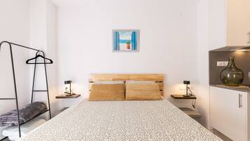 A bedroom with a bed, a hanging clothes rack, bedside tables with lamps, and a wall-mounted picture.