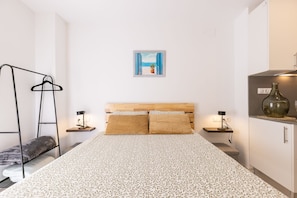 A bedroom with a bed, a hanging clothes rack, bedside tables with lamps, and a wall-mounted picture. - Old Town • Studio - Unik Vacation (Tarragona)
