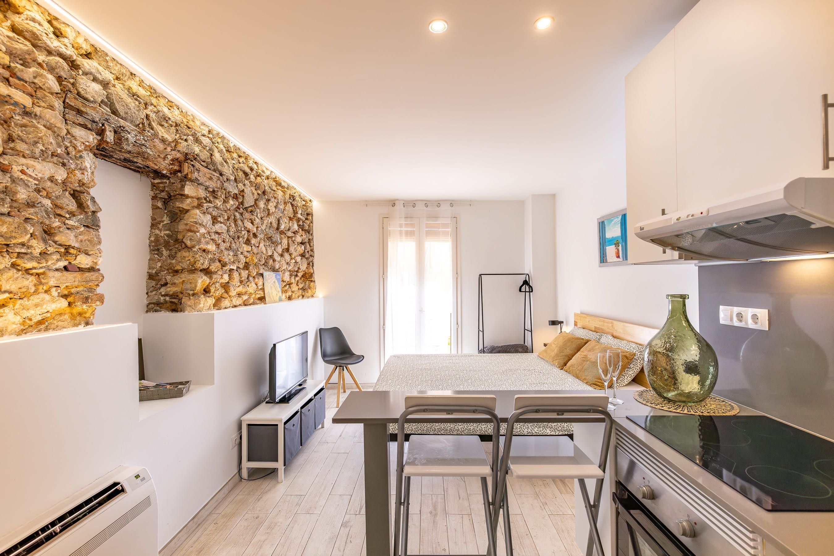 A modern kitchen with a stone wall, a dining area with a table and chairs, a TV, and a large oven.