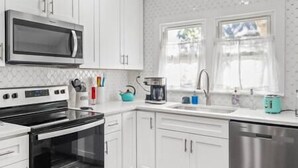 A modern kitchen with white cabinets, a stainless steel dishwasher, a black oven, a coffee maker, and a kettle. - Heart of Fountain Inn: 2BR Gem (Fountain Inn)