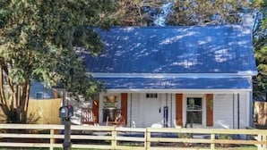 A single-story building with a blue roof, a front porch with a bench, and a small front yard. - Heart of Fountain Inn: 2BR Gem (Fountain Inn)