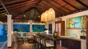 Un espacio de comedor al aire libre con techo de madera, un cuadro grande de tablas de surf y vistas a un jardín exuberante.