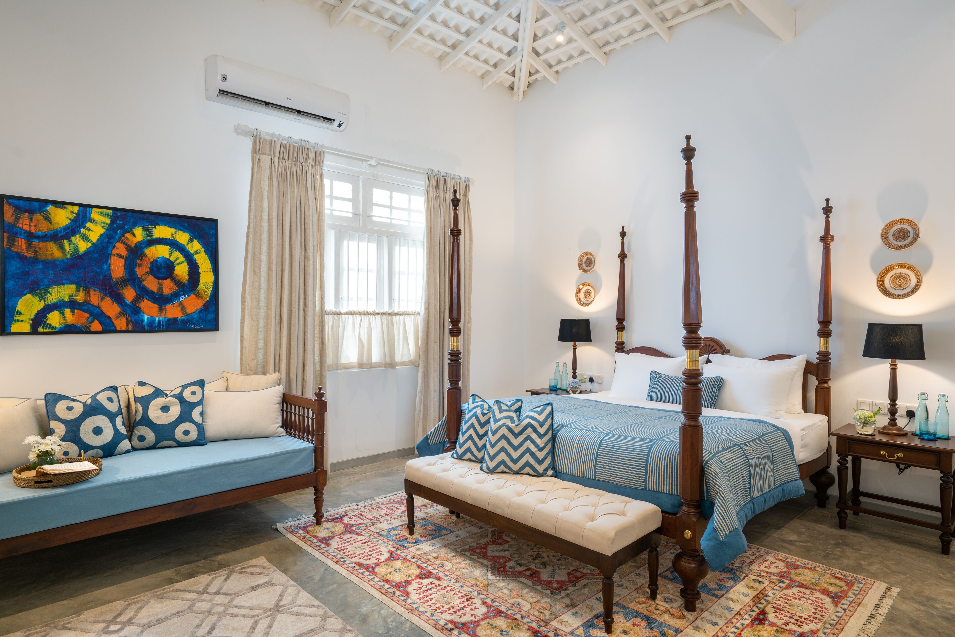 Un dormitorio con cama con dosel, un sofá, un banco y una alfombra colorida.