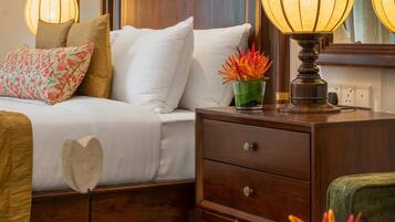 Una cama bien hecha con almohadas blancas y estampadas, una lámpara de noche y una mesita con objetos decorativos.