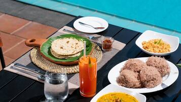 Una mesa con un plato de comida, un vaso de jugo y un bol de salsa junto a una piscina.