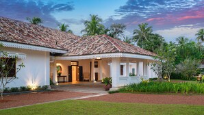 Una casa de dos pisos con techo de tejas, paredes blancas y un jardín con palmeras.