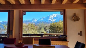 Ein Holzinnenraum mit Tisch und Stühlen, einem Fenster mit Bergblick und einer Wandleuchte.