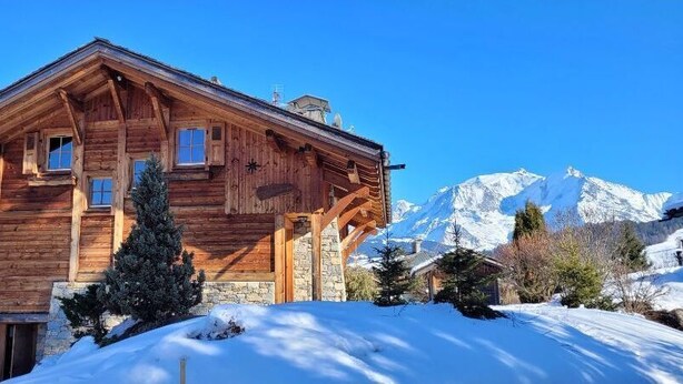 Eine Holzhütte mit Steinunterbau vor einer verschneiten Berglandschaft.