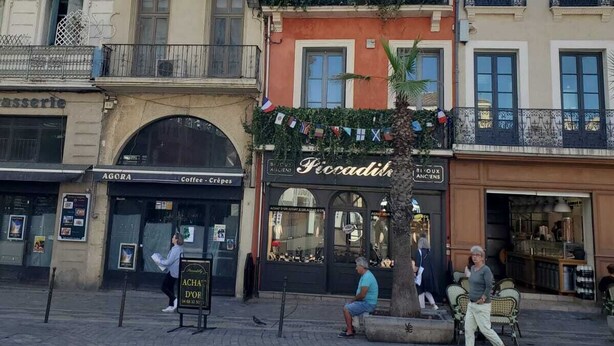 A street with buildings, a café, and a shop with a sign 'Ficadits'. - Appartement Chez Kate & Jack à 5 Minutes à Pied de la Cathédrale Saint Just (Narbonne)