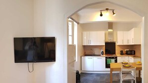 A compact living space with a kitchenette, a dining area, and a TV mounted on the wall. - Appartement Chez Kate & Jack à 5 Minutes à Pied de la Cathédrale Saint Just (Narbonne)
