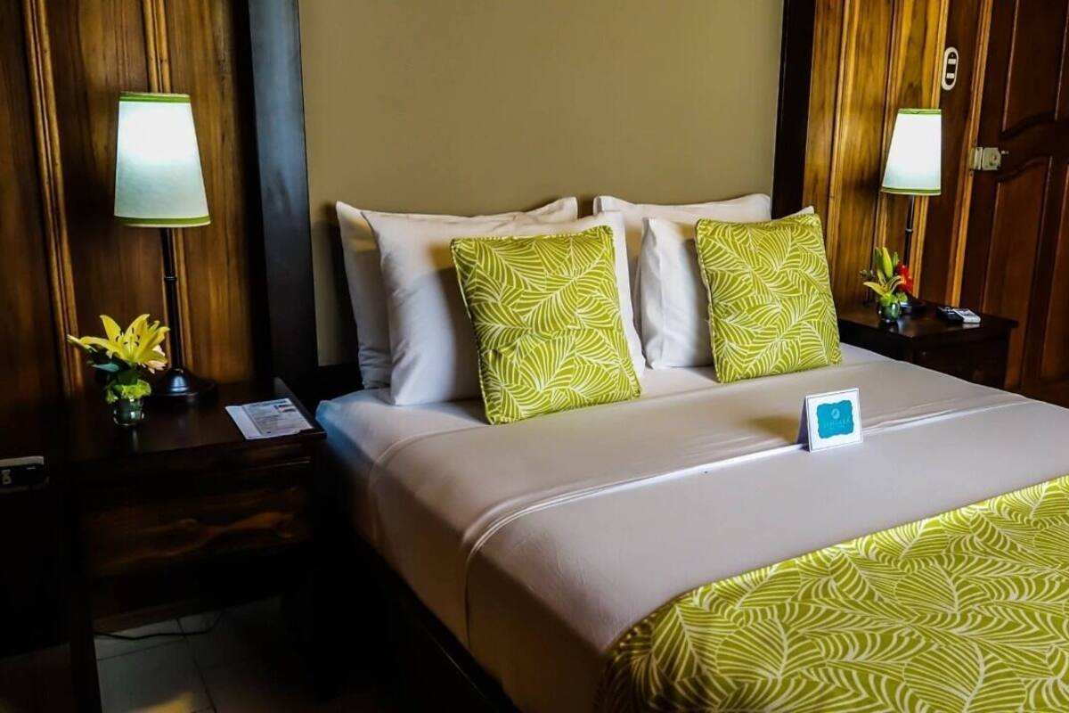 A hotel room with a bed, two nightstands, a lamp, and a small table with a plant.