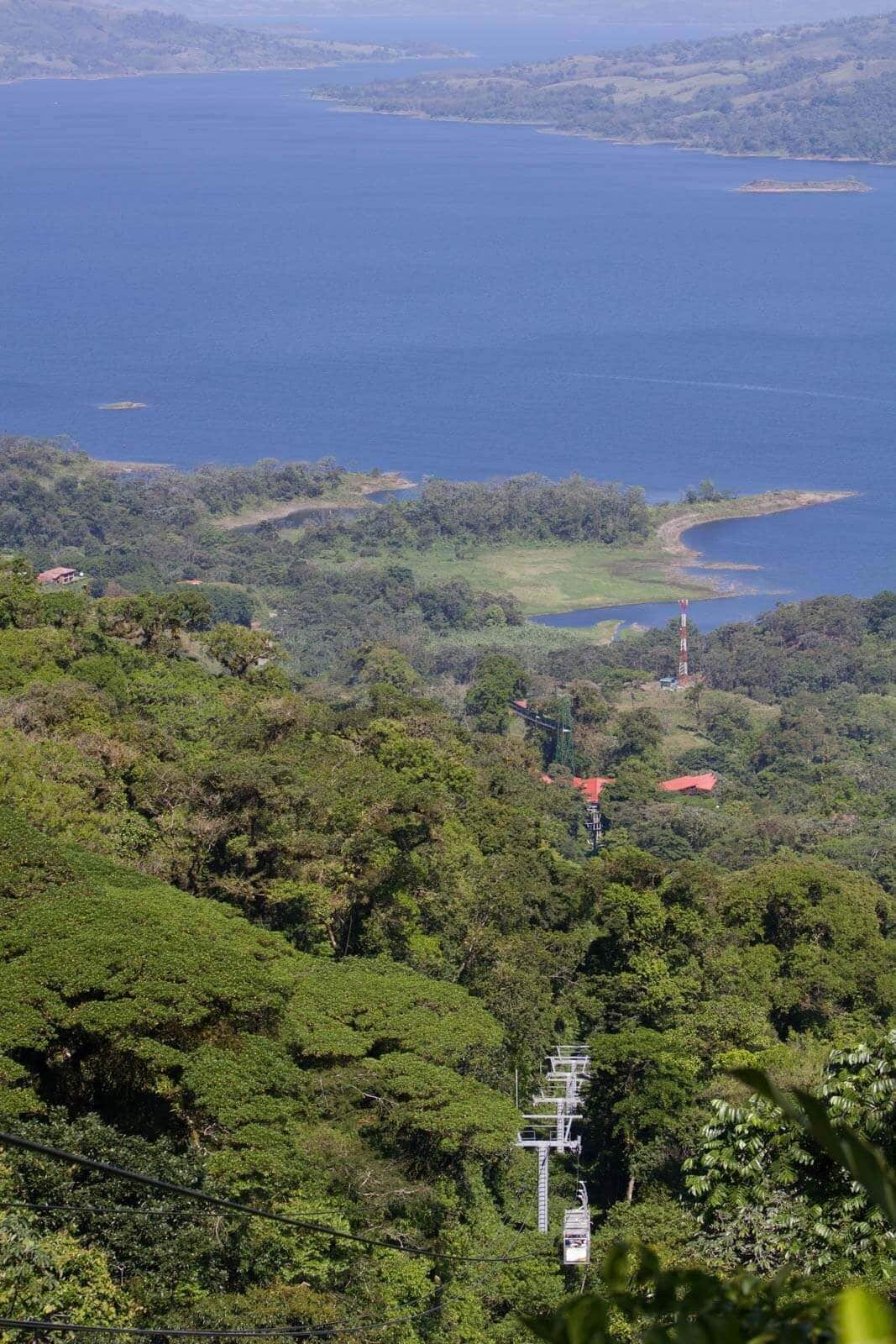 A cable car system in a lush, green landscape with a body of water and distant hills.