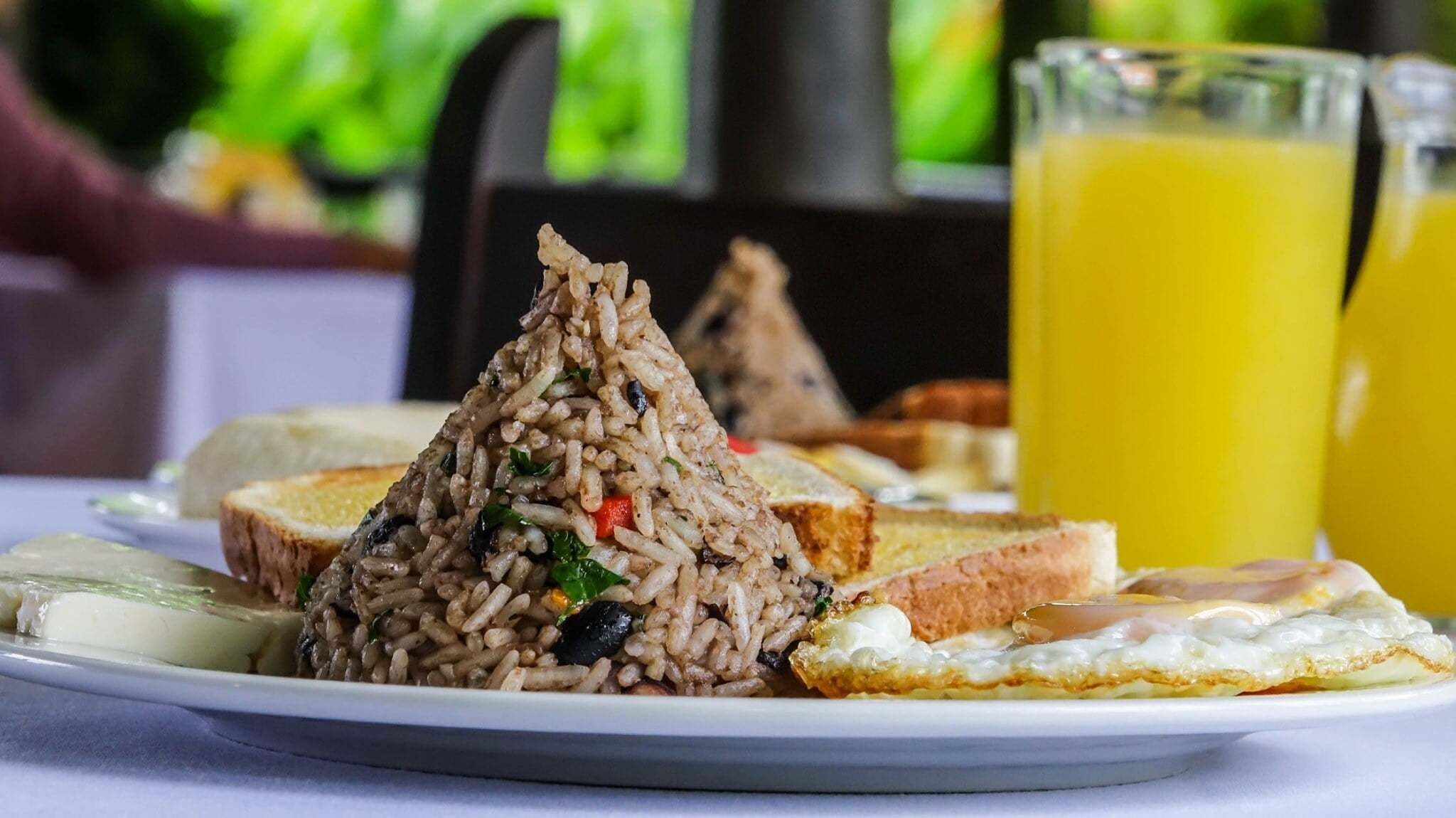 A plate with rice, toast, and a fried egg. There is a glass of orange juice in the background.
