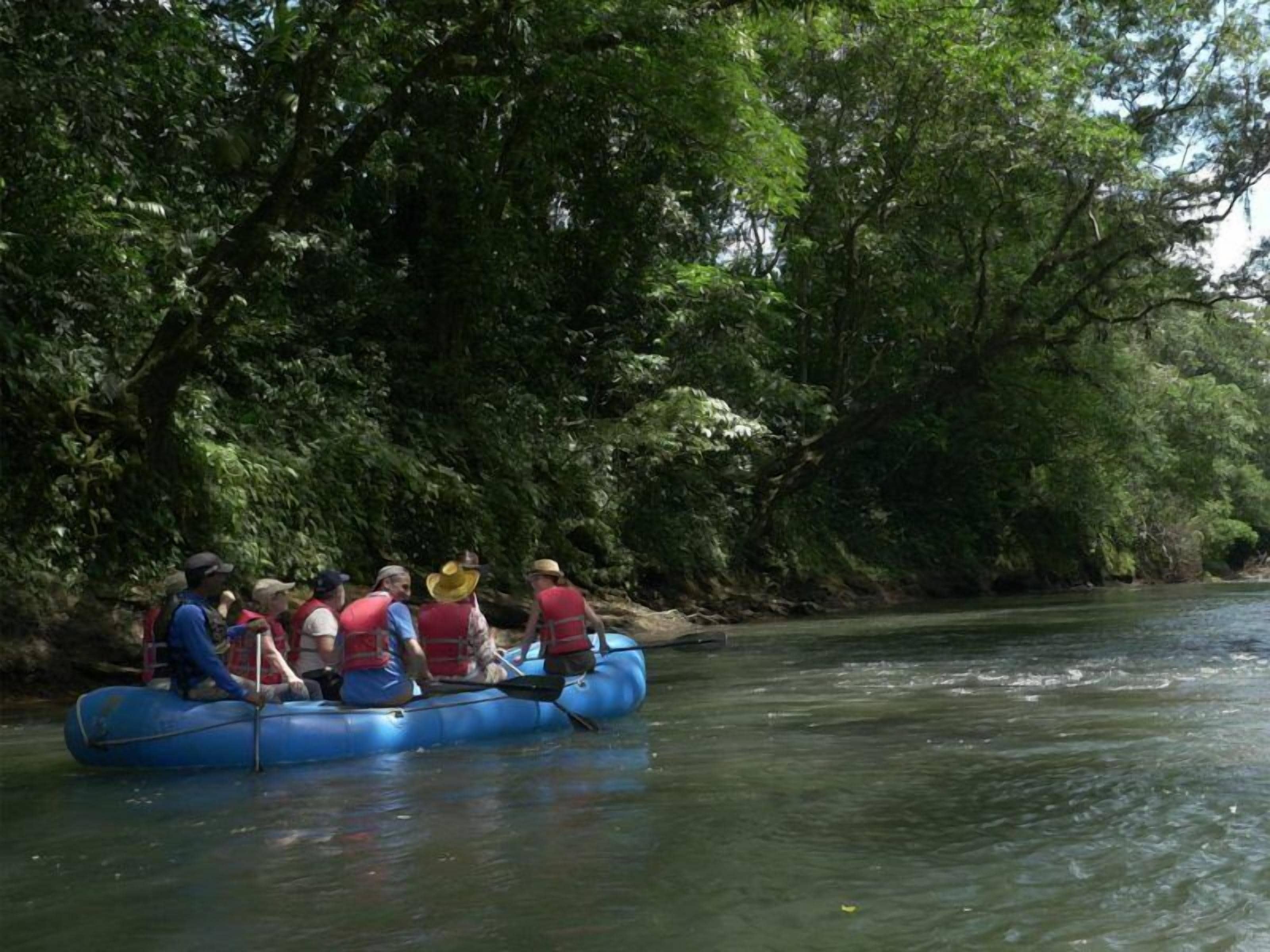 Een groep mensen in een blauwe luchtbed op een rivier, omgeven door weelderige begroeiing.