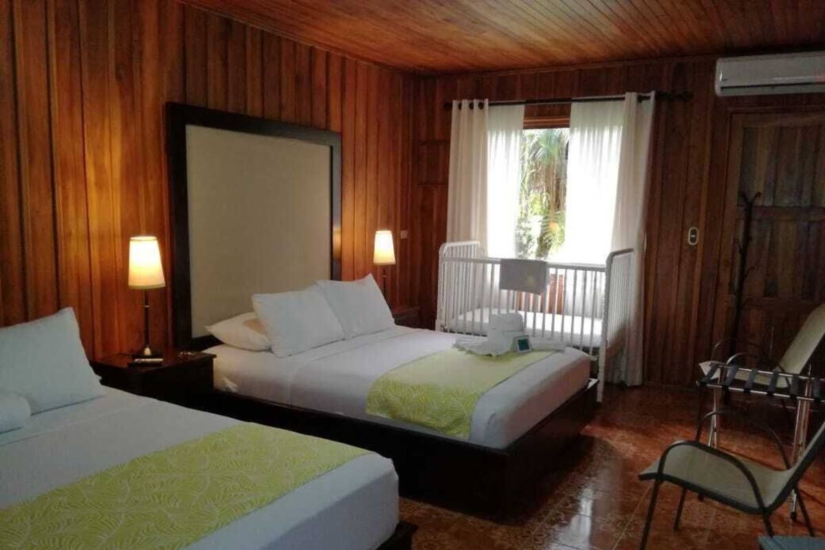 A room with two beds, wooden walls, a balcony, and a chair.