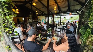 An outdoor restaurant with patrons dining under a covered area with hanging lights.