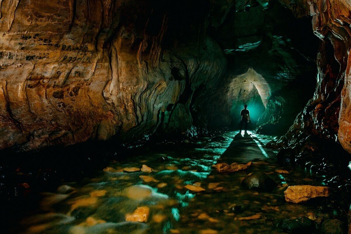 A person standing in a cave with a path leading to a light source.