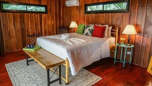 A wooden-paneled room with a bed, two bedside lamps, a small table, and a window.