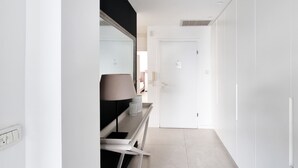 Um corredor estreito com uma porta branca no final, uma luminária e um interruptor na parede.