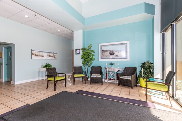 A reception area with a tiled floor, several wicker chairs with green cushions, a potted plant, and a framed picture on the wall.