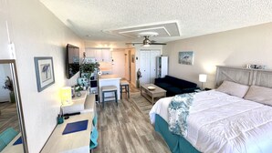 A bedroom with a bed, a desk, a chair, a sofa, and a kitchenette.