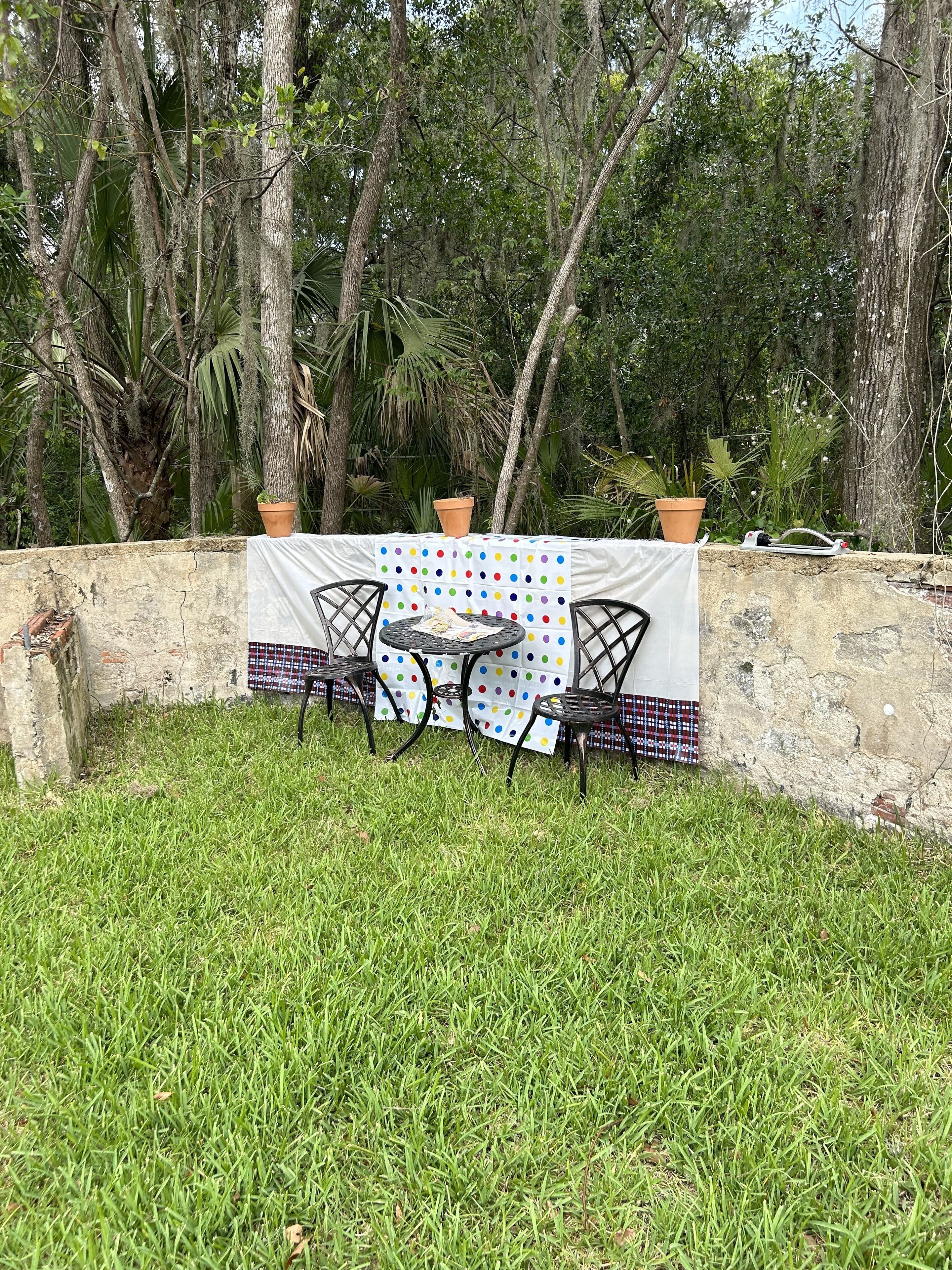 Un espacio de comedor al aire libre con una mesa redonda y dos sillas, rodeado por un mantel blanco con lunares de colores.