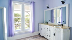 Un baño con un amplio ventanal, un tocador blanco con dos lavamanos y un espejo grande.