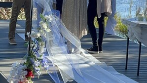 Una ceremonia de boda en una terraza de madera junto a un lago, con un arco blanco y decoración floral.