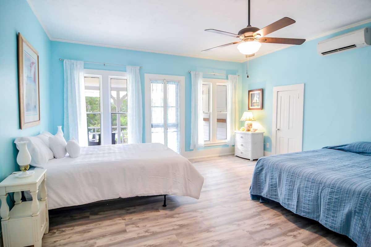 Um quarto com uma cama, mesa de cabeceira, cômoda, ventilador de teto e uma janela com cortinas.