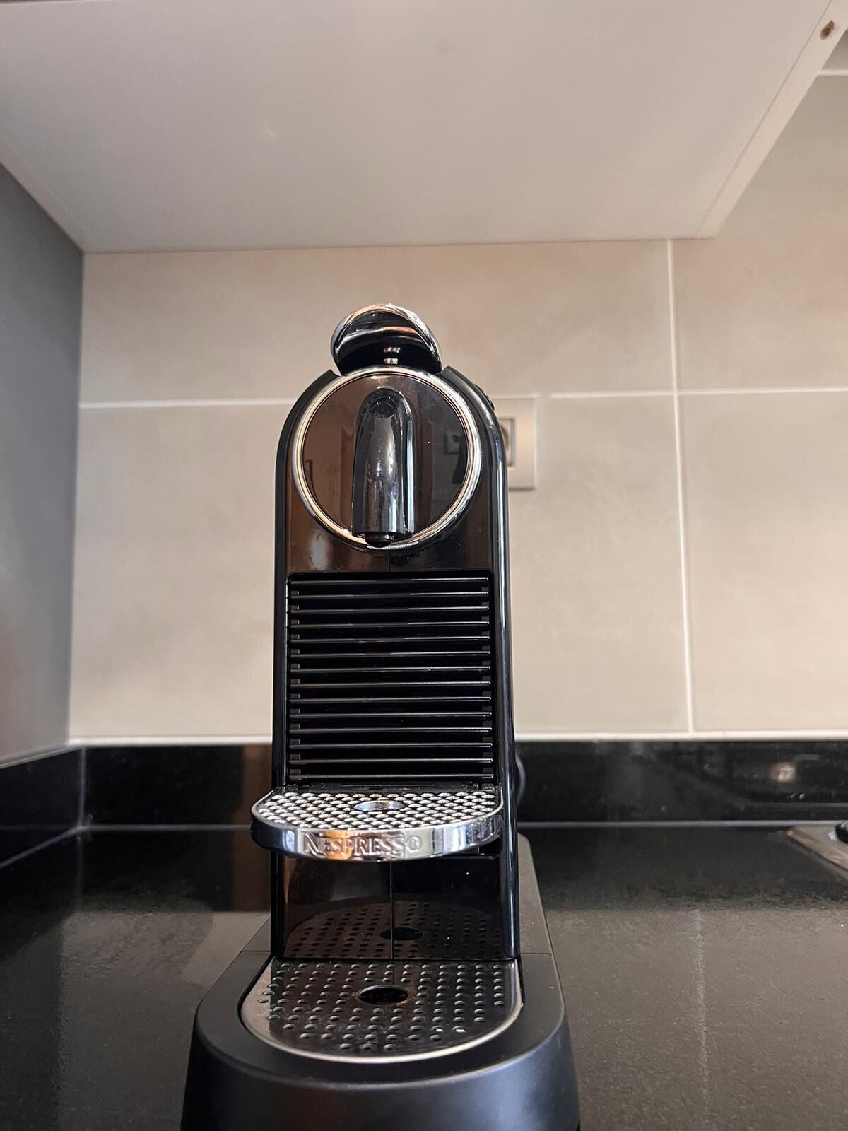 Une machine à expresso noire, dotée d’un bac d’égouttage circulaire et d’un dessus métallique.