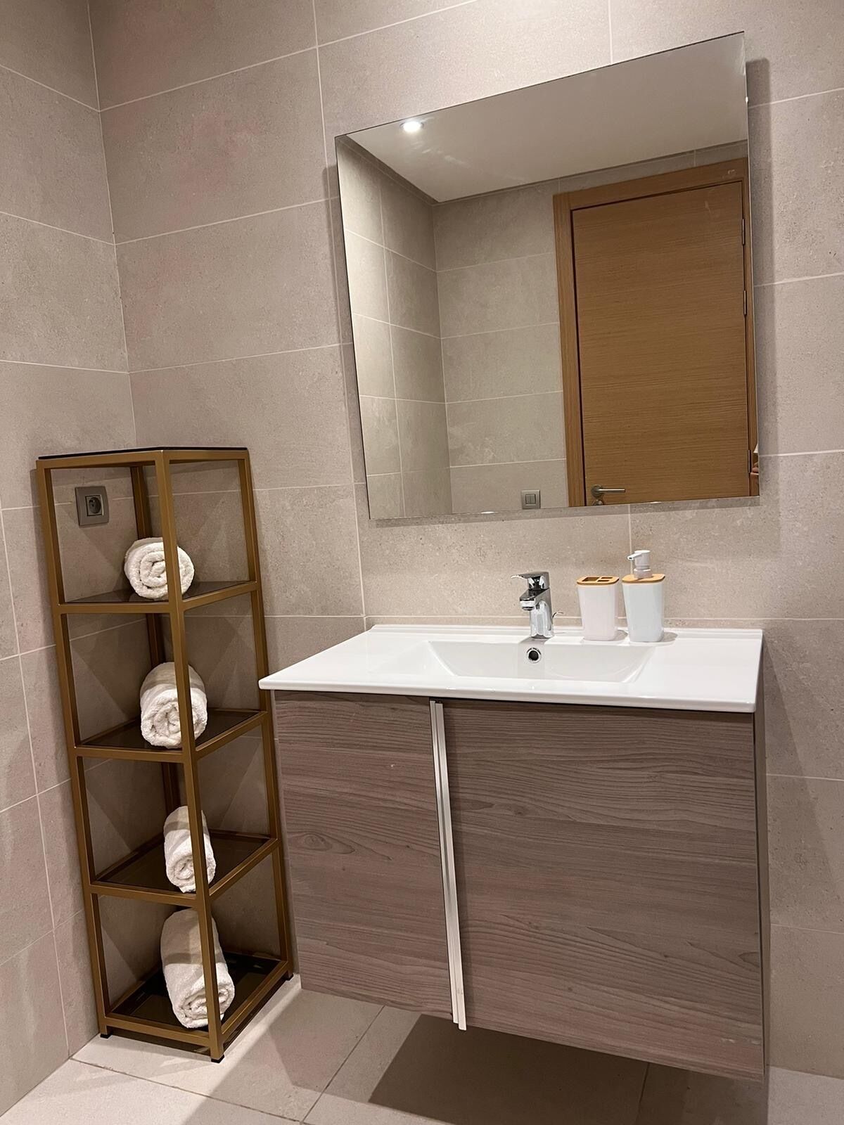 Un baño con lavamanos blanco, mueble de madera y toallero con toallas.