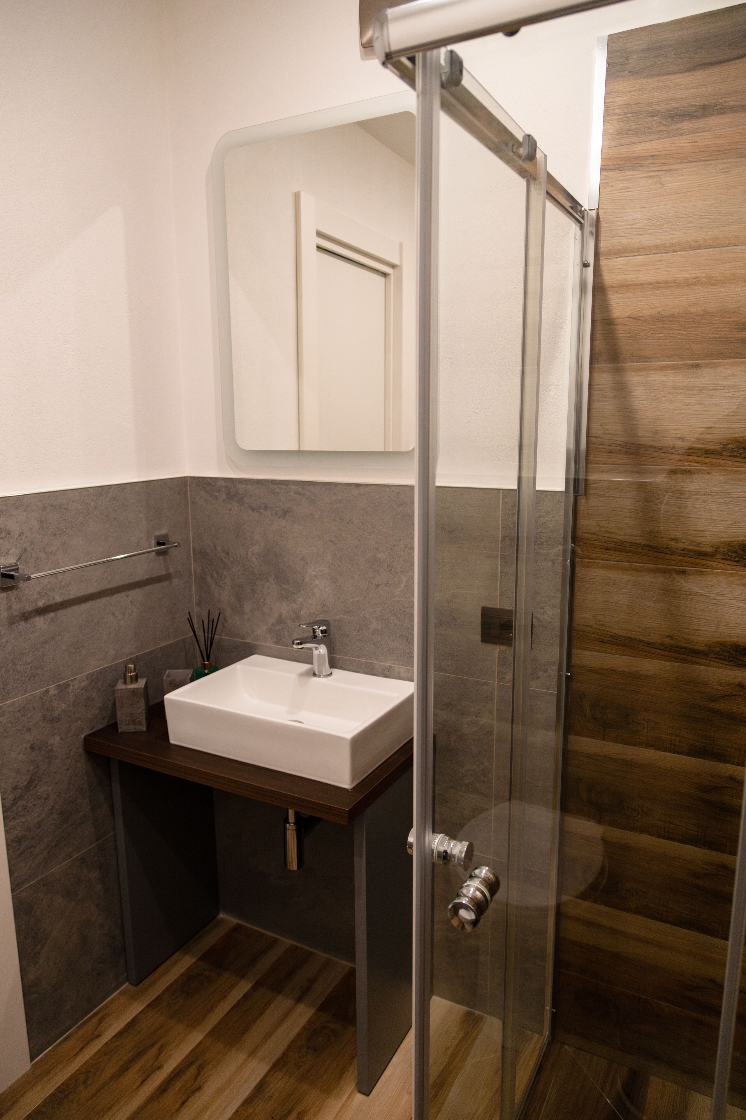A modern bathroom with a glass shower enclosure, a white sink, and a wooden vanity.