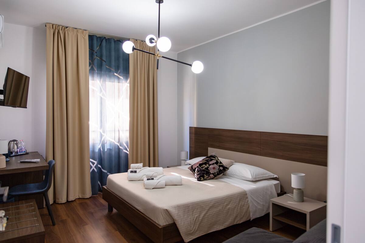 Una habitación de hotel con cama, mesita de noche, lámpara y escritorio con silla.