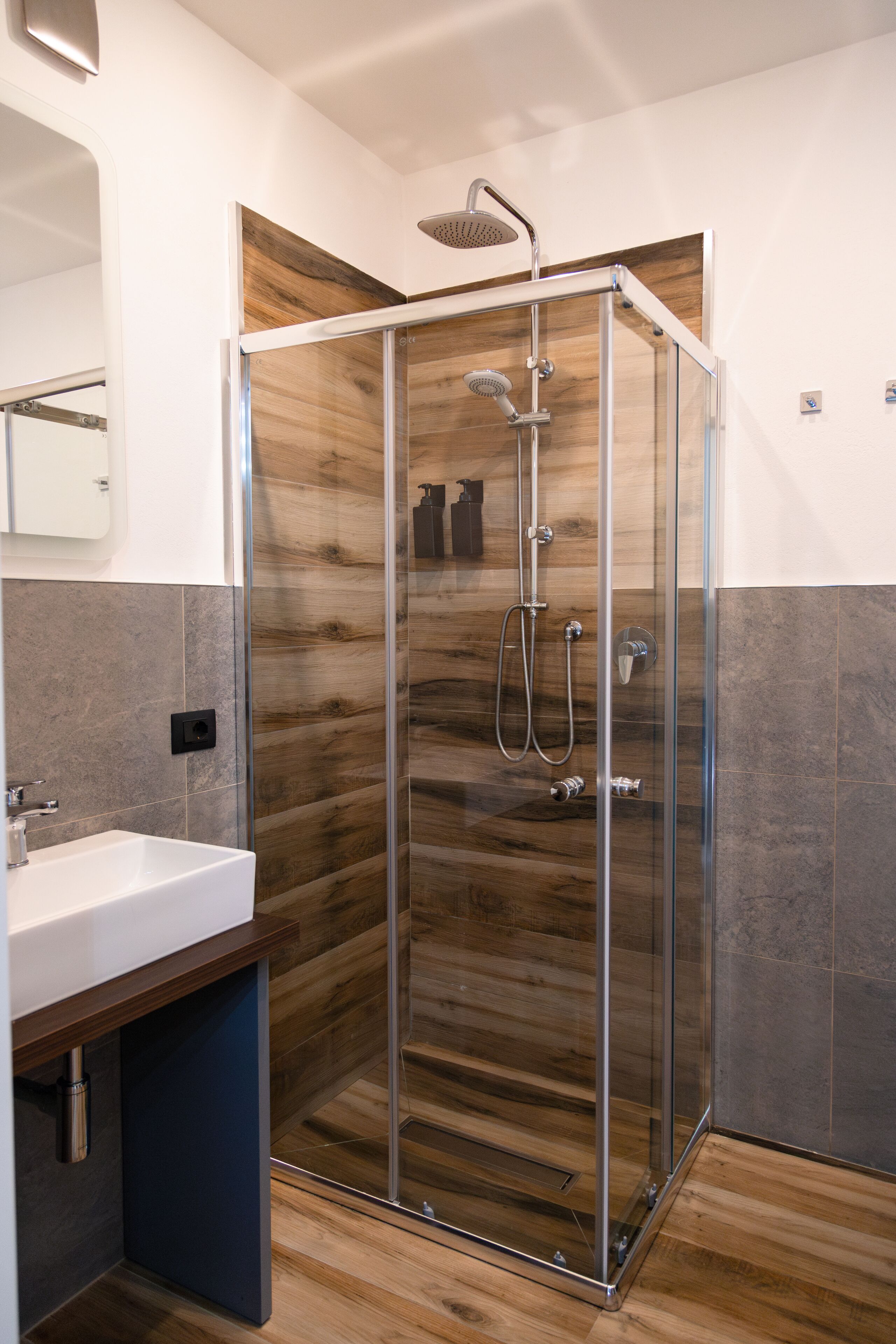 A modern bathroom with a glass-enclosed shower, a white sink, and a wooden vanity.