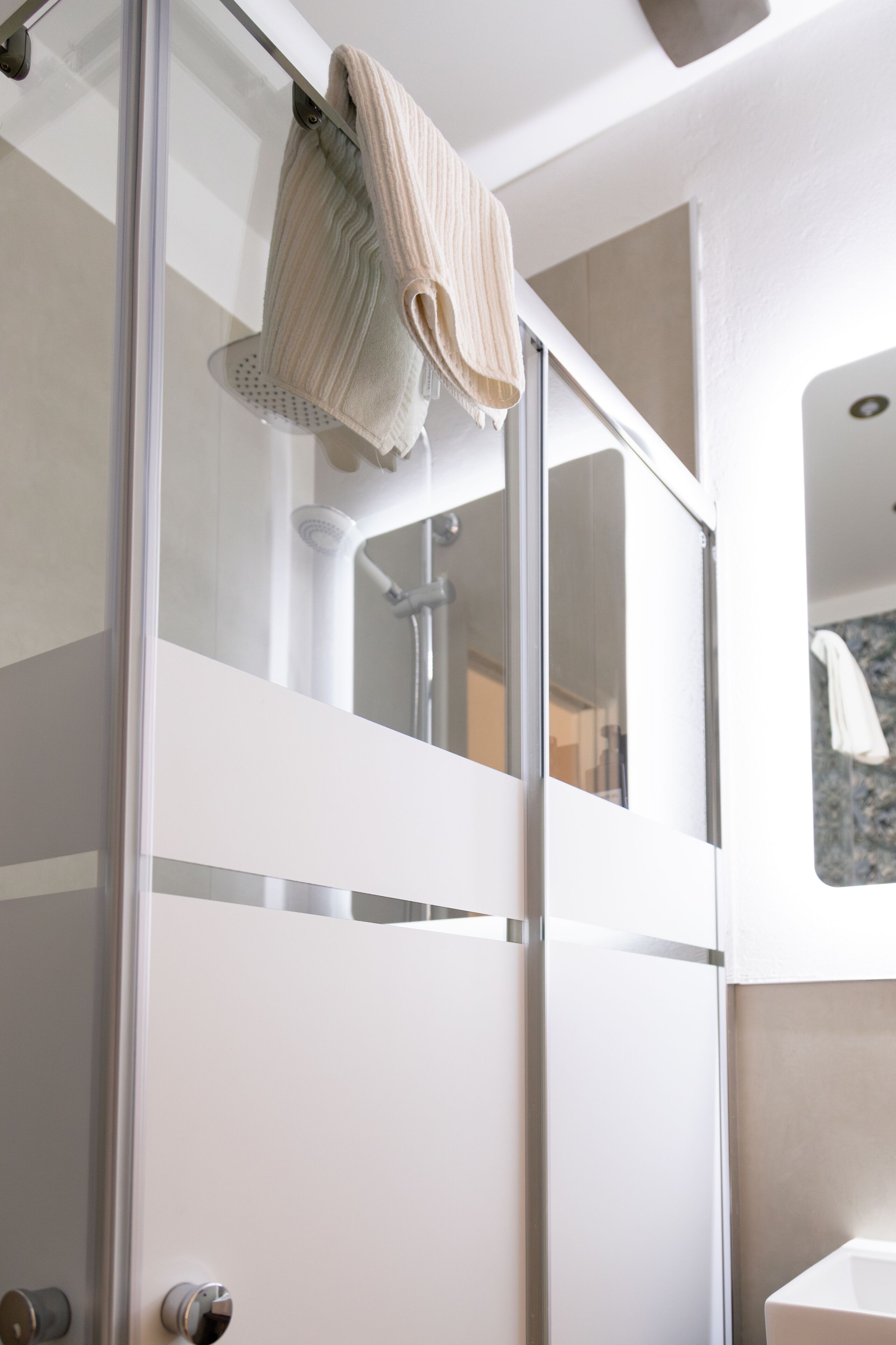 Une salle de bain moderne avec une douche à parois de verre, une serviette suspendue au pommeau de douche et un espace lavabo bien visible.