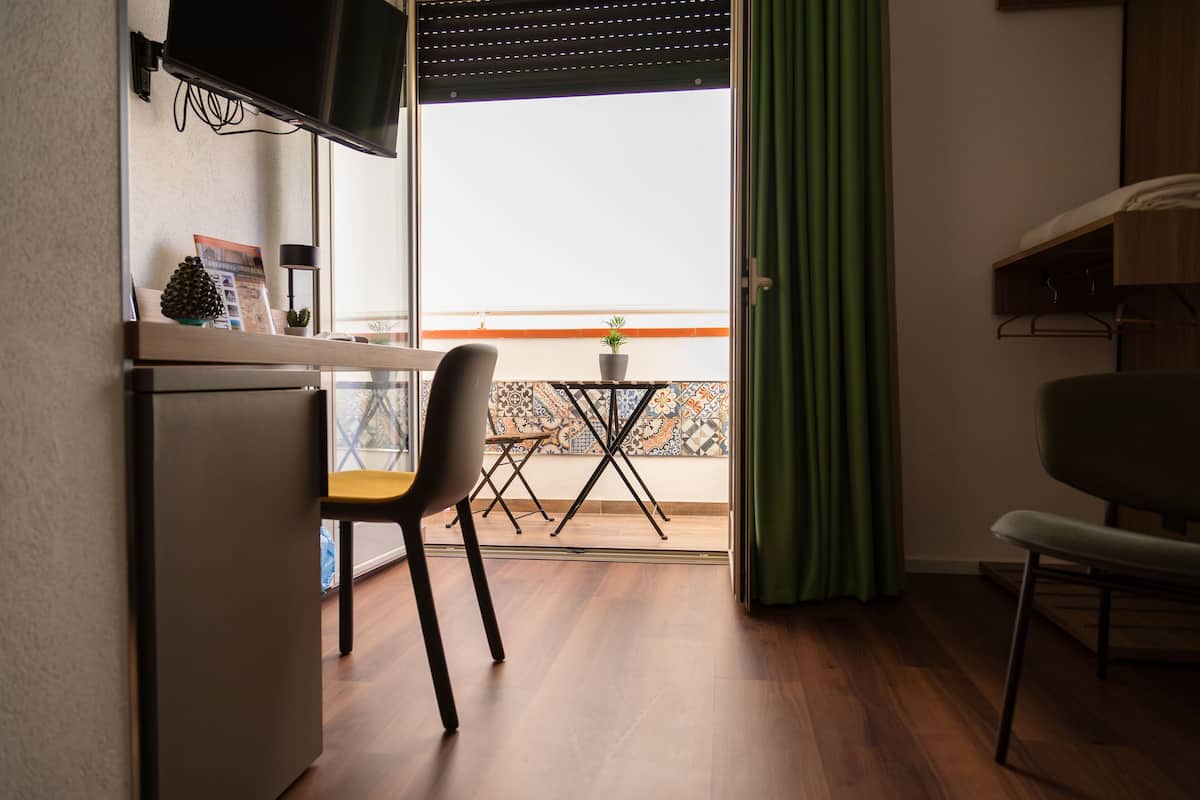 Una habitación compacta con suelo de madera, una mesita con planta en maceta, una silla y un televisor montado en la pared.