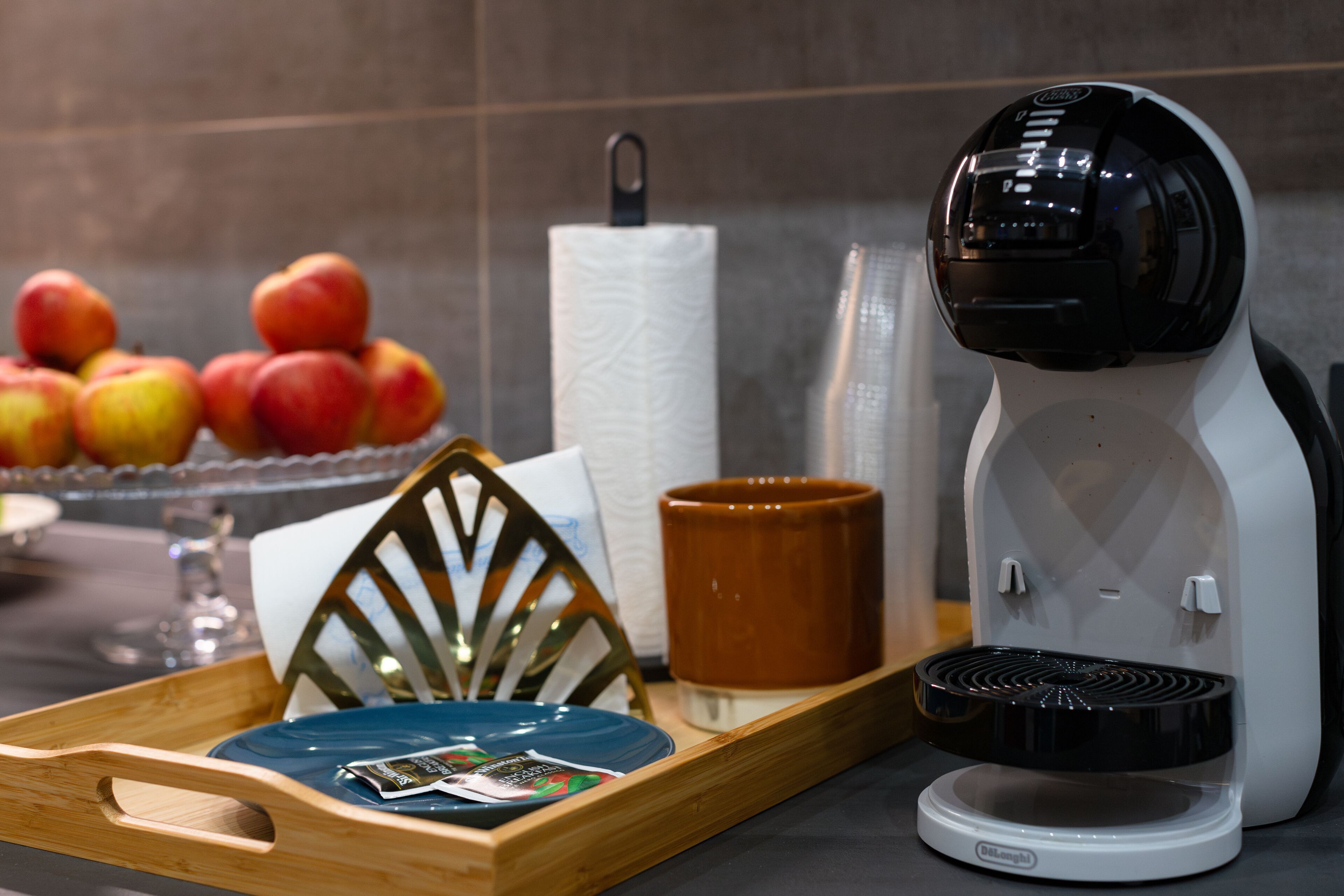A kitchen counter with a coffee maker, a tray with a plate, a mug, and a bowl of fruit.
