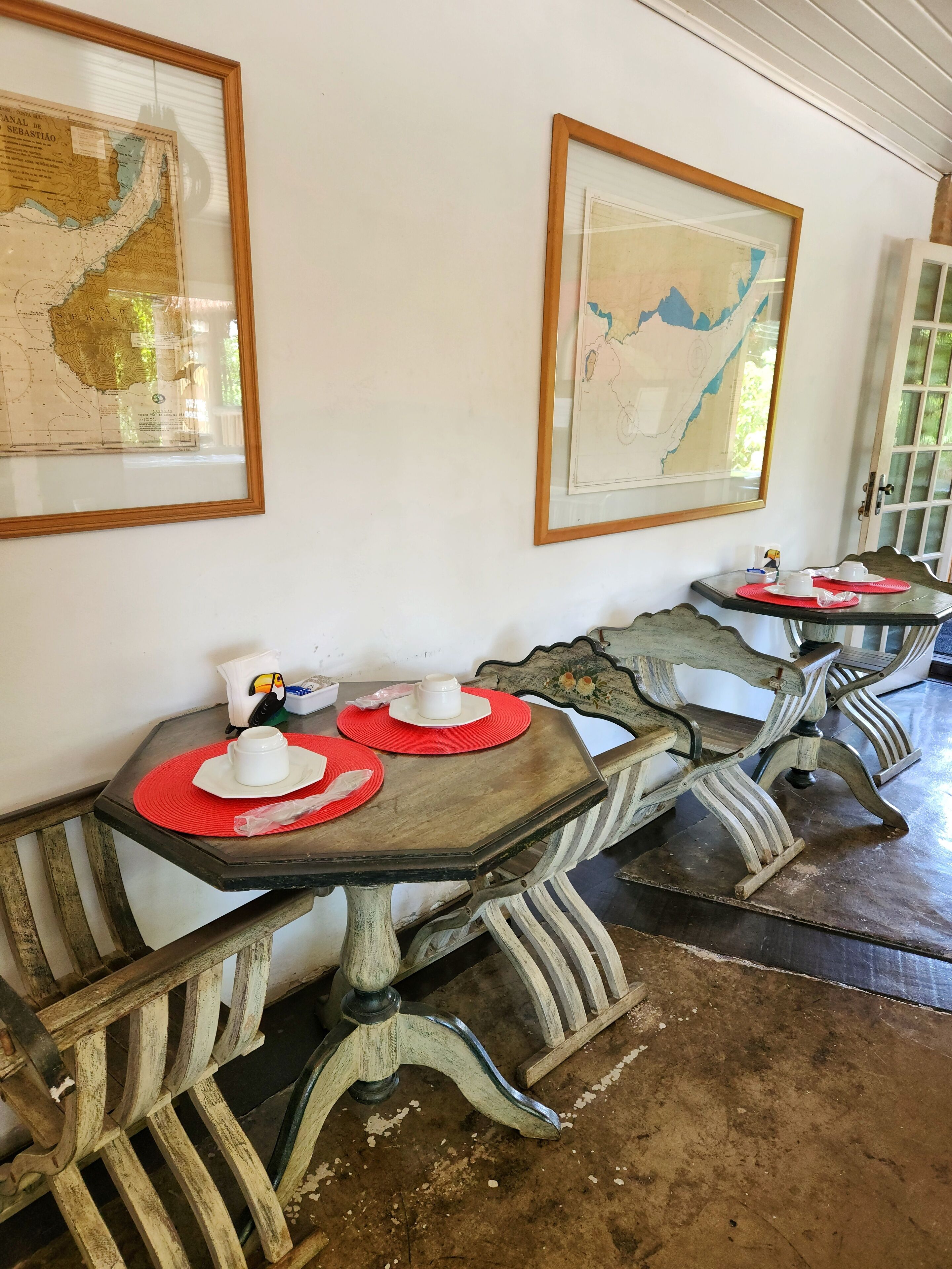 Un coin repas avec des tables et des chaises en bois d’époque, des cartes encadrées accrochées au mur, et une petite table sur laquelle sont posés une théière et des tasses.
