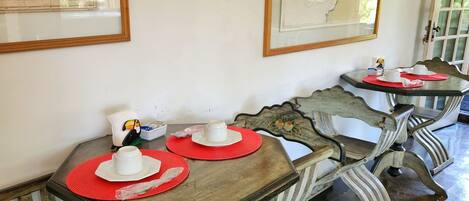 Un coin repas avec des tables et des chaises en bois d’époque, des cartes encadrées accrochées au mur, et une petite table sur laquelle sont posés une théière et des tasses.