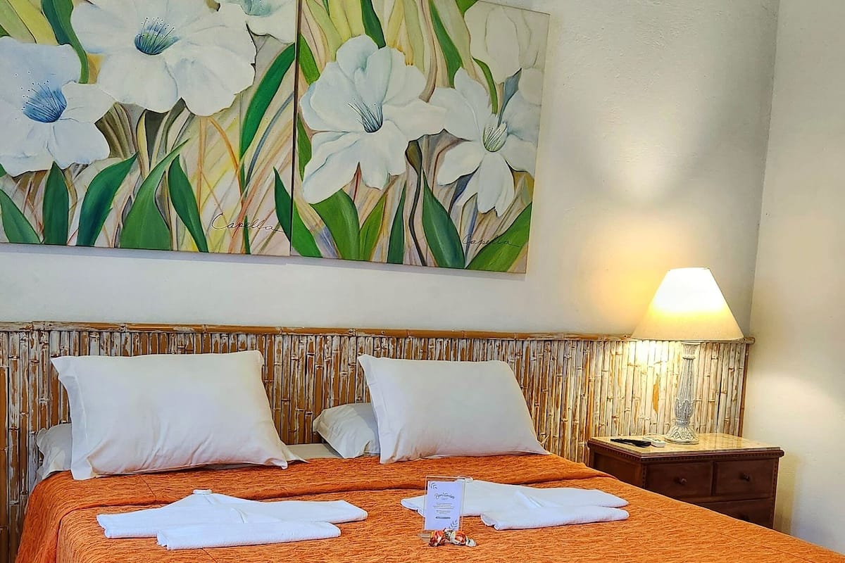 A hotel room with a large bed, two pillows, a nightstand with a lamp, and a wall-mounted air conditioner.