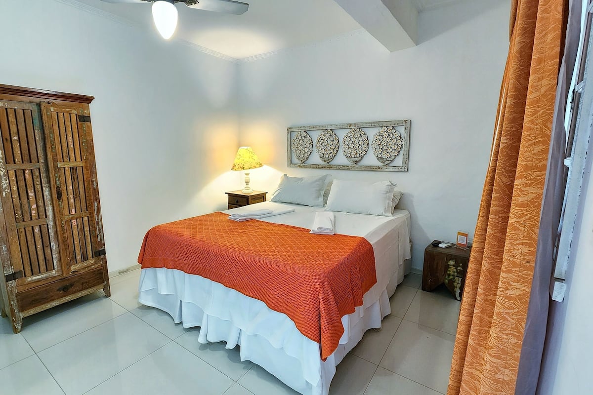 A bedroom with a bed, a nightstand, a lamp, a wall decoration, and a wardrobe.