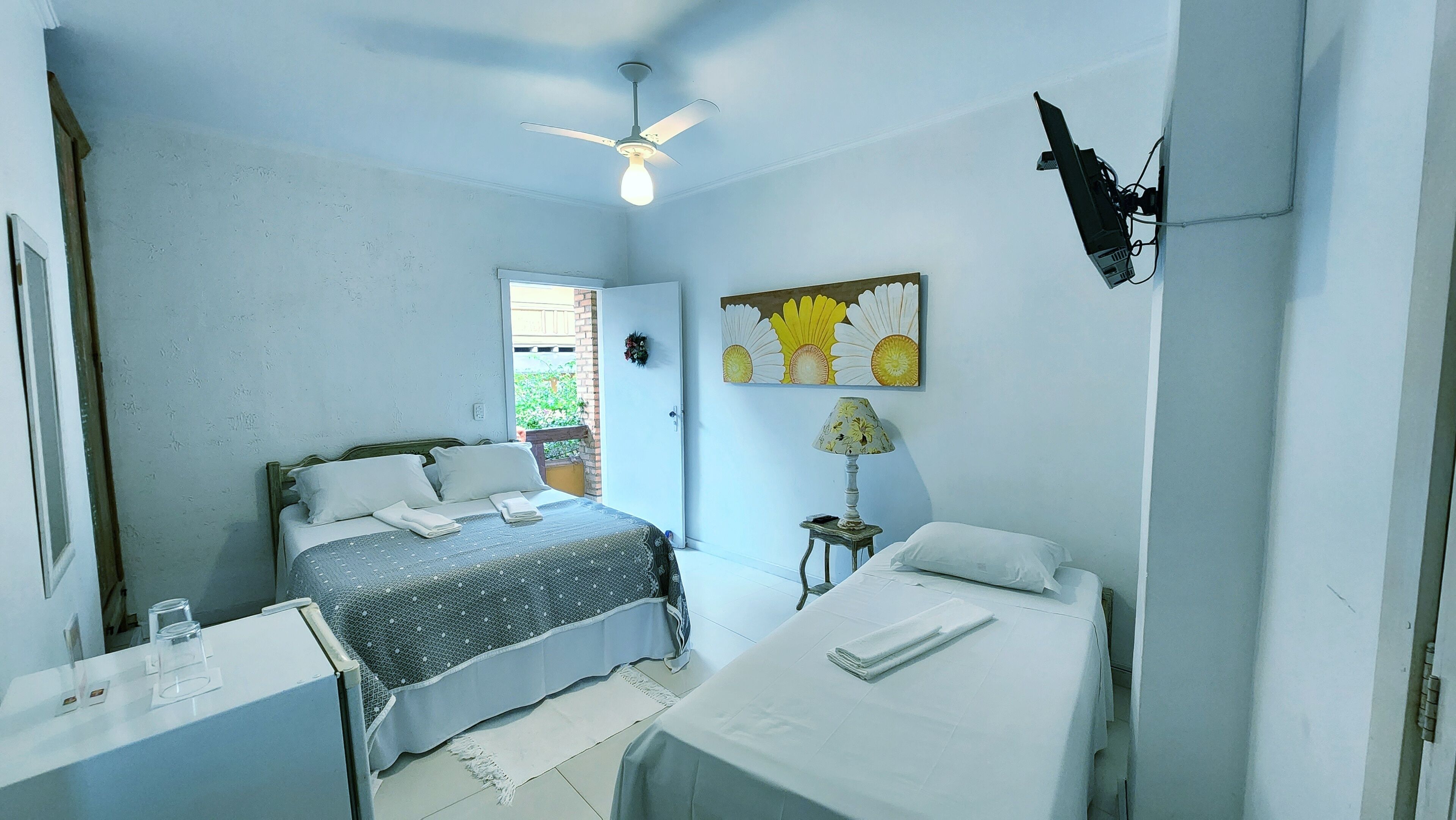 Un dormitorio con una cama, un escritorio, una silla, un ventilador de techo y una ventana.