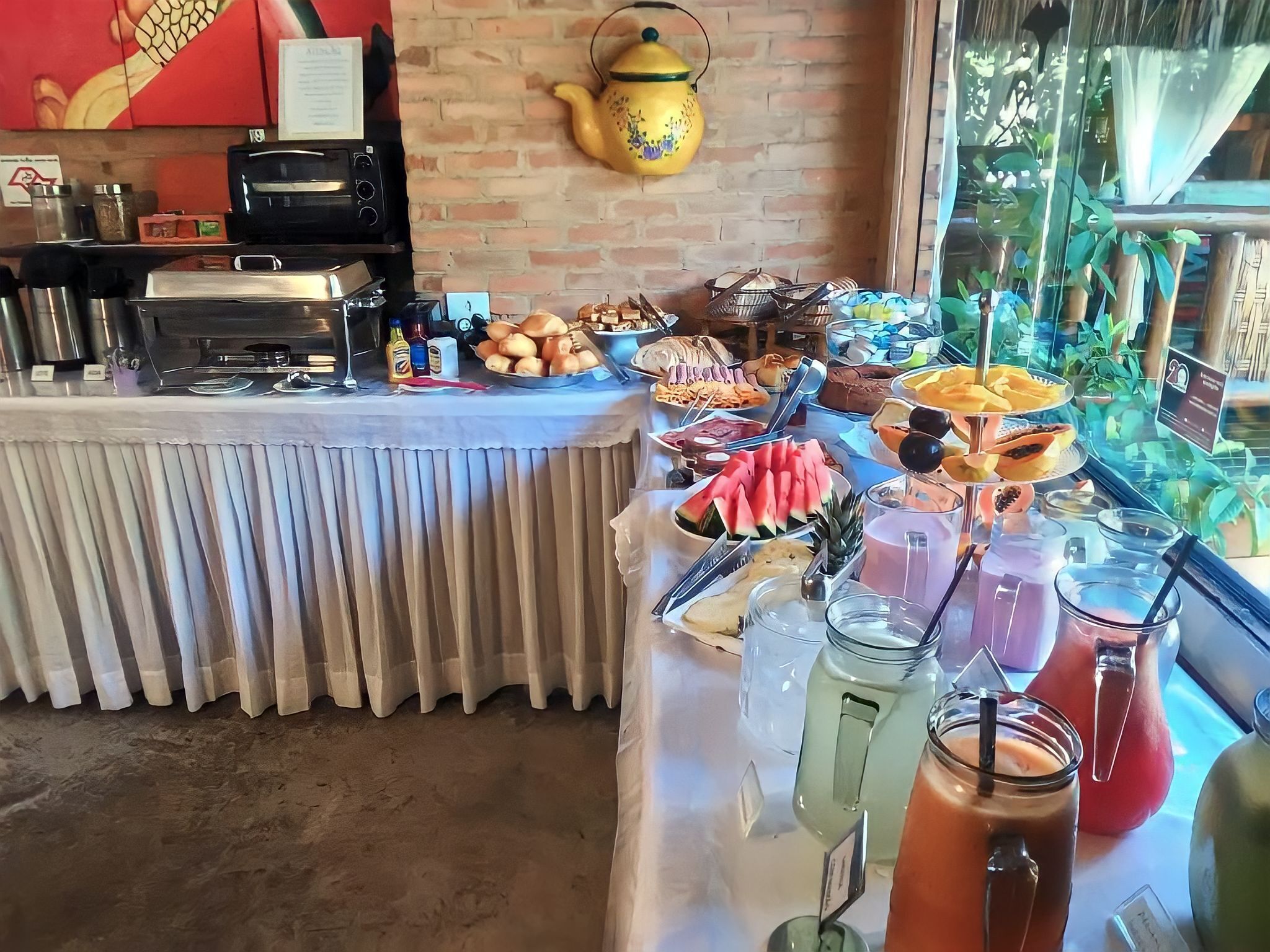 Ein reichhaltiges Buffet mit Speisen und Getränken, eine Ziegelwand und eine Teekanne im Hintergrund.