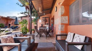 A covered outdoor seating area with wicker furniture, potted plants, and a stone wall.