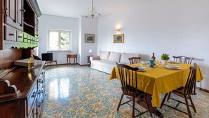 Una zona de menjador amb estovall d'una taula groga, cadires de fusta, un sofà i un paviment amb motius.